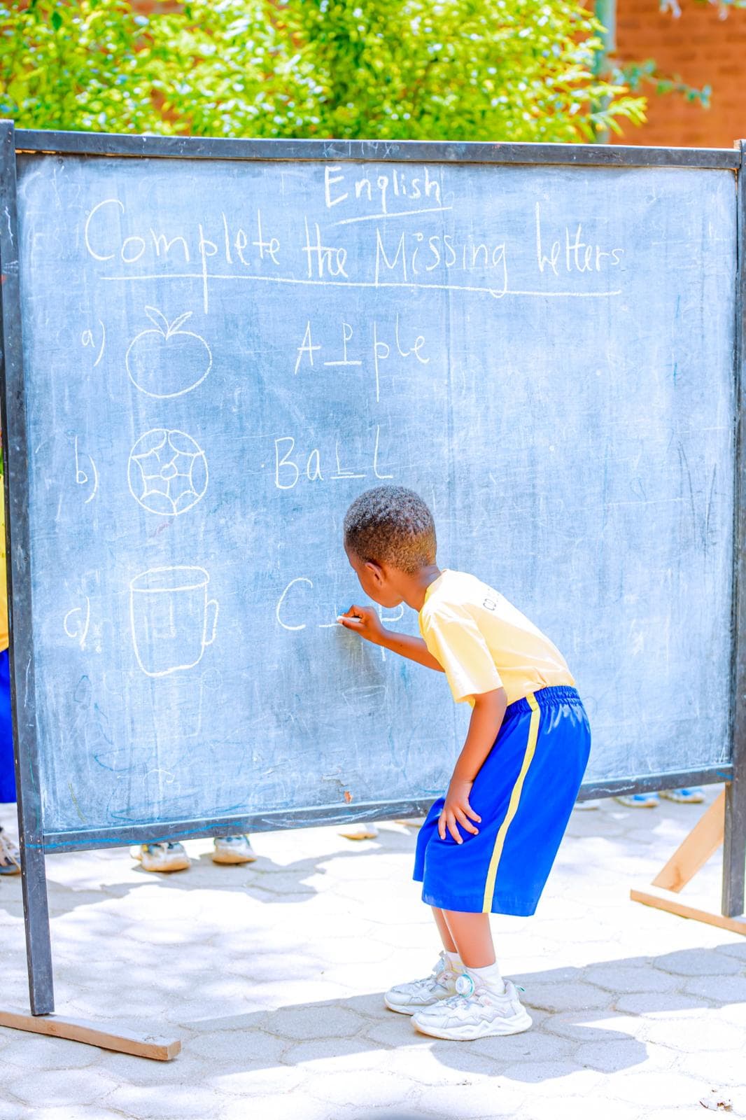A child completing missing letters on a chalkboard during an English class
