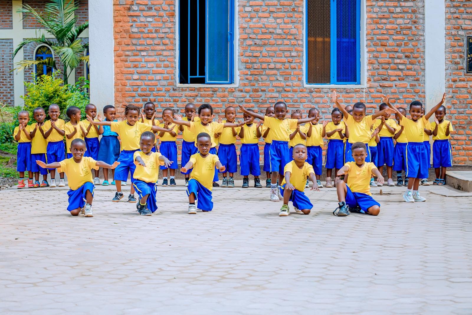 Children of ECD Musezero standing in their yellow and blue uniforms outside a primary school in Rwanda